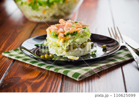 Layered salad of cabbage and other vegetables with pieces of red fish in a plate. Layered salad of cabbage and other vegetables with pieces of red fish in a plate. 110625099