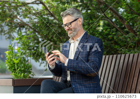 Mature corporate professional in a suit engaged with his smartphone, portraying connectivity and business on the go. Mature corporate professional in a suit engaged with his smartphone, portraying connectivity and business on the go. 110625673