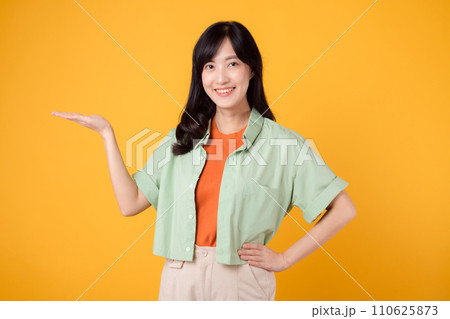 Vibrancy and joy portrait Asian young woman wears pastel green shirt on orange shirt and show happy smile while pointing hand gesture to free copy space. Perfect for adding lively touch to projects. Vibrancy and joy portrait Asian young woman wears pastel green shirt on orange shirt and show happy smile while pointing hand gesture to free copy space. Perfect for adding lively touch to projects. 110625873