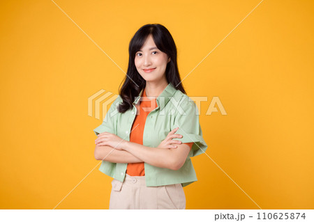 Radiate confidence portrait of Asian woman wears green shirt on orange shirt and show happy smile while confidently crossing her arms. Perfect for capturing sense of self assurance and empowerment. 110625874
