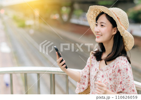 young asian woman traveler with weaving basket using mobile phone and standing on overpass with railway background. Journey trip lifestyle, world travel explorer or Asia summer tourism concept. young asian woman traveler with weaving basket using mobile phone and standing on overpass with railway background. Journey trip lifestyle, world travel explorer or Asia summer tourism concept. 110626059