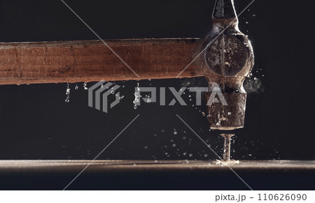 An old hammer hits a nail close-up on dark background. Dust rises from the impact. Carpentry concept. 110626090