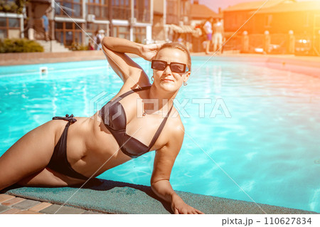 Bikini-clad woman enjoys poolside relaxation. Poolside ambiance. Capturing woman's relaxed time near pool. 110627834