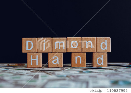 Wooden blocks with the text "Dimond Hand" on a black background and crypto banknotes scattered on the ground. 110627992