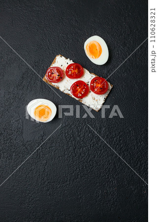 Ingredients for sandwich with boiled egg, cherry tomatoes, canned tuna, garlic and spices over black grunge background. Top view Ingredients for sandwich with boiled egg, cherry tomatoes, canned tuna, garlic and spices over black grunge background. Top view 110628321