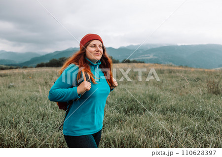 Woman holding phone in mountains, view from behind. Road trip, transport, travel, technology and people concept. High quality photo 110628397