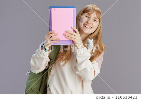 smiling trendy girl with backpack peeking out of notebooks 110630423