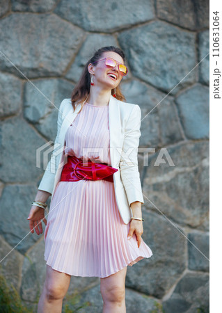 happy stylish woman in pink dress and white jacket in city 110631064