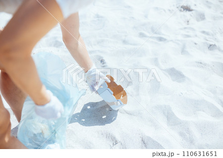 Closeup on woman volunteer on ocean shore collecting garbage Closeup on woman volunteer on ocean shore collecting garbage 110631651