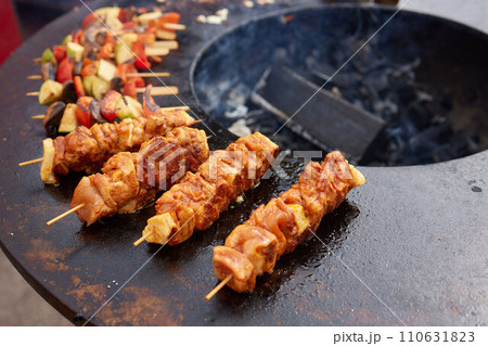 Round grill in the shape of a bowl with fire inside. A man prepares a hearth for barbecue. The round hearth is cleaned before cooking. The firewood lies in the bowl of the outdoor hearth. 110631823