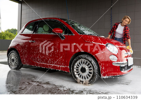 Blonde young woman washing a car and feeling positive 110634339
