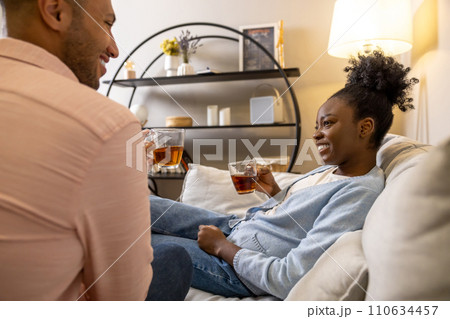 Couple talking drinking tea from glasses sitting on sofa in living room 110634457