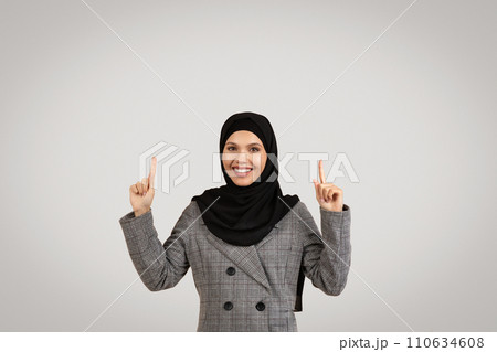 Happy hijab-wearing businesswoman pointing upwards at free space 110634608