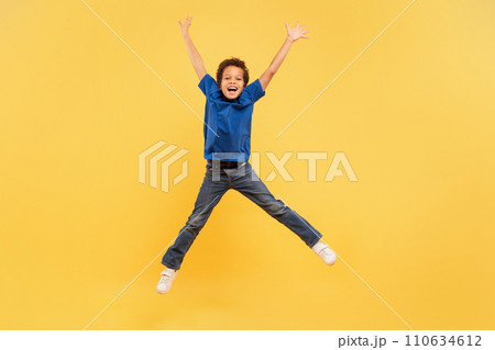 Ecstatic boy jumping high with arms up on yellow background Ecstatic boy jumping high with arms up on yellow background 110634612