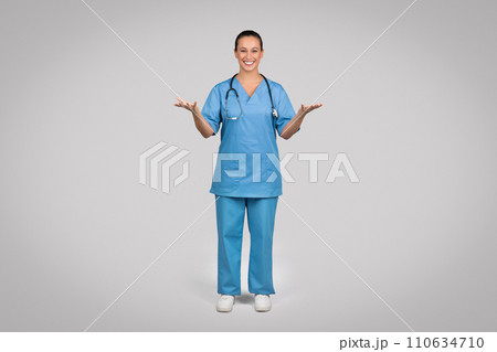 Smiling female doctor wearing blue medical uniform coat and stethoscope talking to camera, explaining and gesturing 110634710