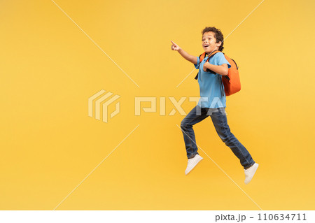 Boy in mid-stride pointing excitedly, yellow backpack 110634711