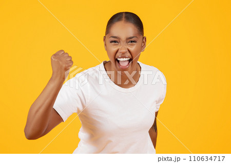 Portrait of emotional black lady making winner gesture, yellow background 110634717