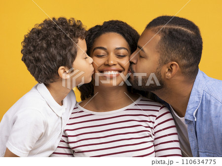 Adorable son and husband giving kisses on cheeks of smiling black mother Adorable son and husband giving kisses on cheeks of smiling black mother 110634775