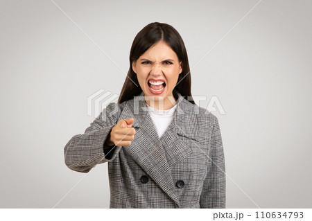 Angry woman in blazer pointing and shouting, frustration evident 110634793