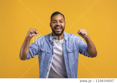 Joyful young black man celebrating success on yellow studio background 110634807