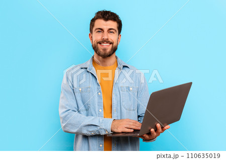 Cheerful guy posing with laptop computer over blue studio background 110635019