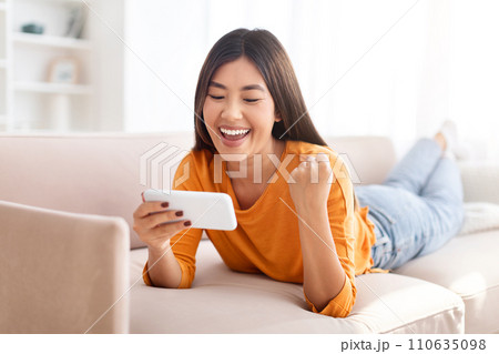 Emotional young asian woman gaming online, using smartphone 110635098