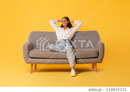 Relaxed black teenager girl resting sitting on couch, yellow backdrop Relaxed black teenager girl resting sitting on couch, yellow backdrop 110635131