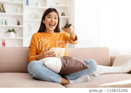 Excited young asian woman watching her favorite TV show Excited young asian woman watching her favorite TV show 110635206