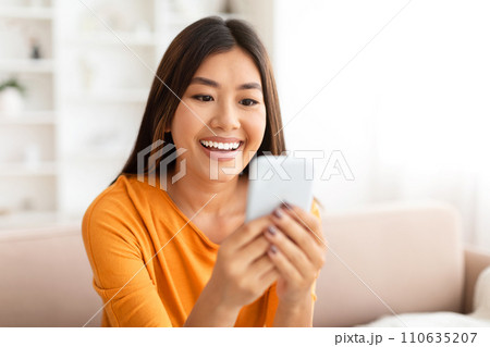Closeup of smiling young asian woman using smartphone at home, 110635207