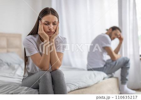 Disappointed lady sitting on bed, ignoring offended man, frustrated wife thinking about relationship problems, 110635217