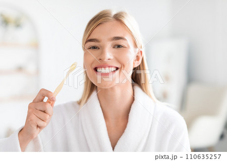 European blonde woman maintaining oral health brushing teeth in bathroom 110635257