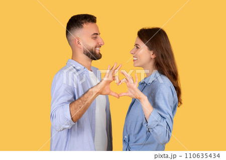 Couple making heart shape with hands, sharing joyful moment on yellow Couple making heart shape with hands, sharing joyful moment on yellow 110635434