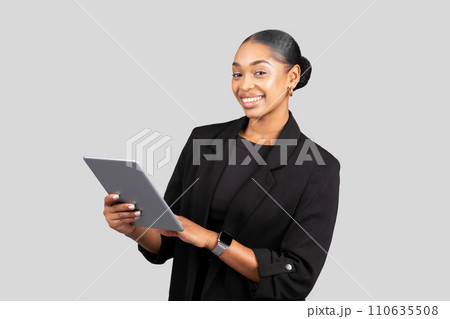 A confident young woman in business attire smiles while holding a tablet 110635508