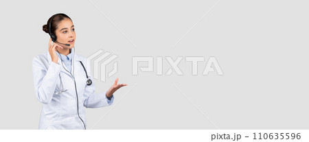 A focused female doctor with a headset speaks to a patient, gesturing informatively 110635596