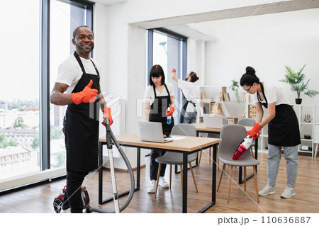 Side view of African American man using vacuum cleaner to clean floor from dirt. 110636887