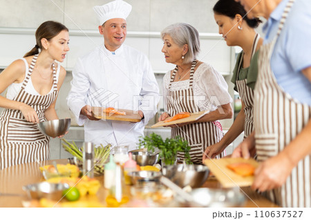 Smiling middle-aged man chef of cooking course teaching attendees how to cook salmon Smiling middle-aged man chef of cooking course teaching attendees how to cook salmon 110637527