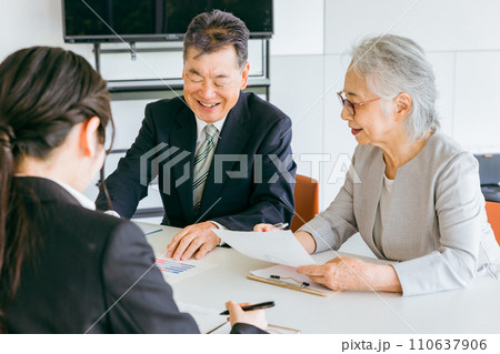 資料を確認する笑顔の高齢者夫婦（M&A・事業譲渡・株式譲渡） 110637906