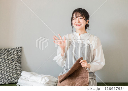 タオルを畳みながら手を振る笑顔の主婦（おかえりなさい・新婚・挨拶） 110637924