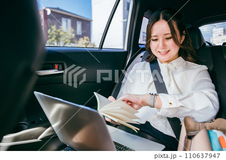 自動車の後部座席でスケジュール時間を確認するアジア人ビジネスウーマン（約束・多忙・時間） 110637947