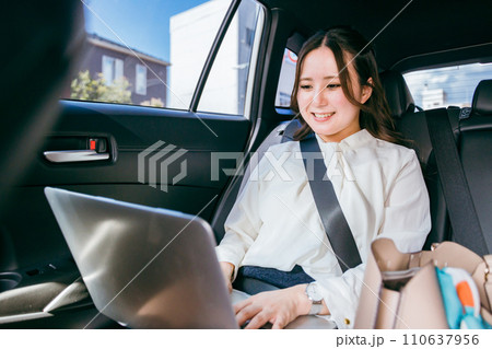 自動車の後部座席でノートパソコンで仕事をするビジネスウーマン(Web会議・オンライン会議・出張) 自動車の後部座席でノートパソコンで仕事をするビジネスウーマン(Web会議・オンライン会議・出張) 110637956