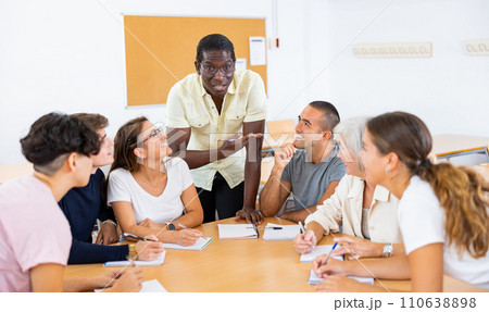 African american male teacher, together with students of different ages, conducts intensive classes at round table in university auditorium 110638898