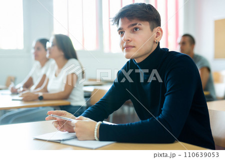 Cheerful young guy student sitting at lecture in university classroom Cheerful young guy student sitting at lecture in university classroom 110639053