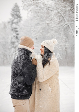Young man and woman hugging and kissing outdoors. Romantic couple at winter in warm jackets walk in the park and hugging. Man and woman wearing winter clothes and knitted hats. Young man and woman hugging and kissing outdoors. Romantic couple at winter in warm jackets walk in the park and hugging. Man and woman wearing winter clothes and knitted hats. 110639065
