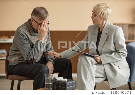 Portrait of mature man crying in therapy session with caring female psychologist supporting him, copy space 110640271