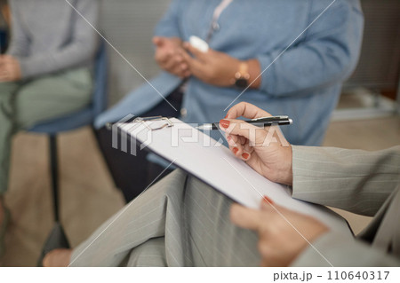 Closeup of unrecognizable female therapist holding clipboard and pen taking notes in support group session, copy space Closeup of unrecognizable female therapist holding clipboard and pen taking notes in support group session, copy space 110640317