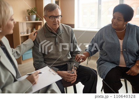 Portrait of senior man sharing mental health struggles in support group session with people comforting him Portrait of senior man sharing mental health struggles in support group session with people comforting him 110640328