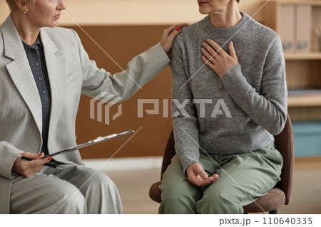 Side view closeup of senior woman sharing mental health struggles with psychologists in therapy session and holding hand to chest, copy space 110640335