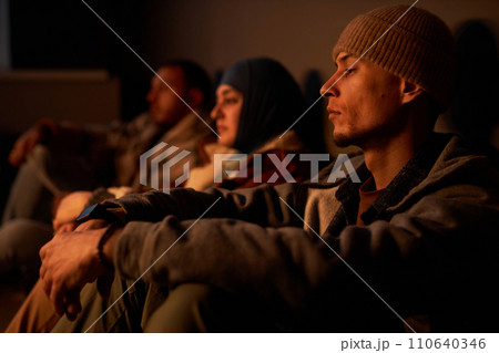 Diverse group of Middle Eastern people hiding in dark bomb shelter with young man in foreground Diverse group of Middle Eastern people hiding in dark bomb shelter with young man in foreground 110640346