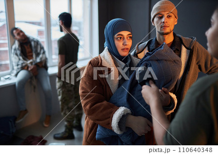 Waist up portrait of Middle Eastern refugee couple with baby talking to microphone while giving interview in shelter, copy space Waist up portrait of Middle Eastern refugee couple with baby talking to microphone while giving interview in shelter, copy space 110640348