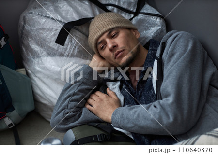 High angle portrait of Middle Eastern young man lying on floor at refugee shelter and looking away with sadness 110640370
